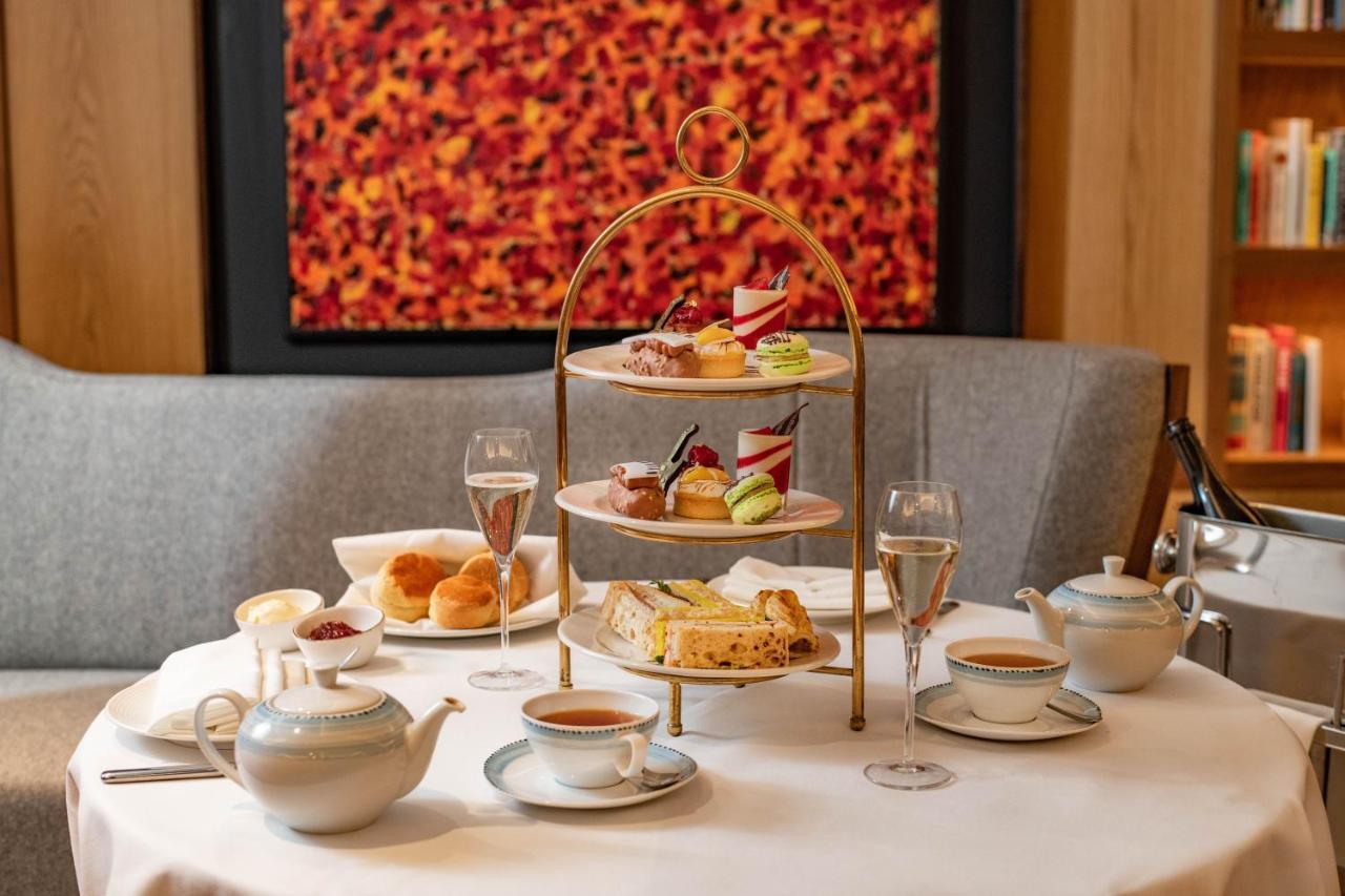 Middle Eight - Covent Garden - Preferred Hotels And Resorts Лондон Екстериор снимка The photo shows an elegant afternoon tea setup on a white tablecloth. At the center, there is a multi-tiered stand displaying a variety of pastries and desserts, including cakes and colorful sweets. Surrounding the stand are teapots and teacups, read