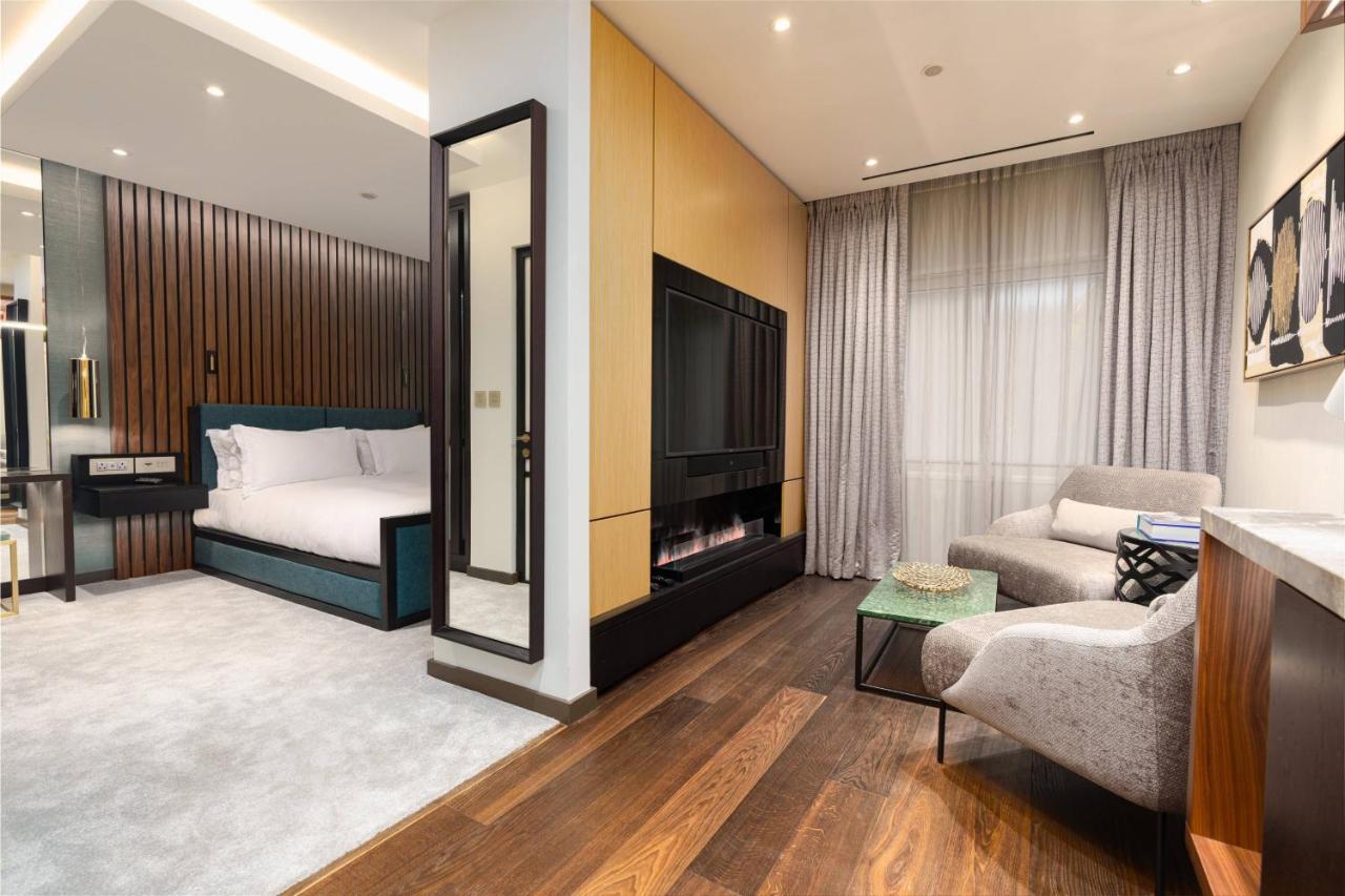 Middle Eight - Covent Garden - Preferred Hotels And Resorts Лондон Екстериор снимка The photo depicts a modern hotel room or suite featuring a cozy living space. On one side, there's a comfortable bed with plush bedding, positioned against a backdrop of elegant wooden paneling. Adjacent to the bed is a contemporary fireplace integra