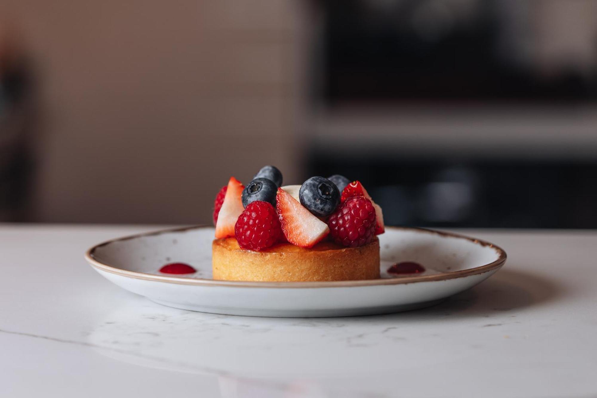 Middle Eight - Covent Garden - Preferred Hotels And Resorts Лондон Екстериор снимка The photo shows a delicious-looking dessert on a white plate. The dessert appears to be a small tart or cake topped with fresh strawberries, raspberries, and blueberries. It has a golden crust, and there are small dollops of a red sauce or fruit pure